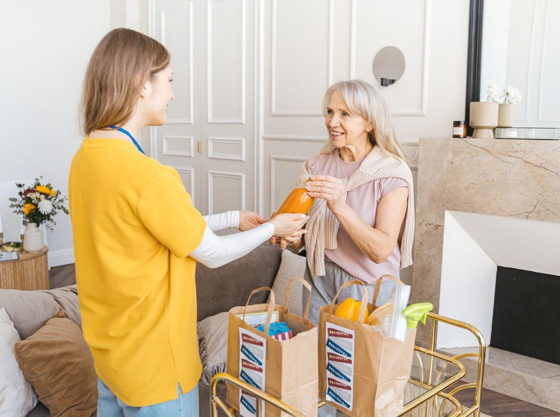 A home health aide bringing groceries to a happy senior woman