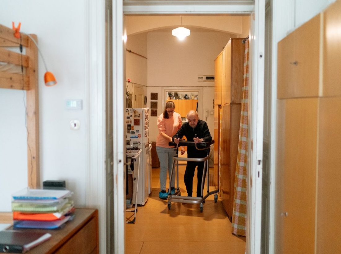 A caregiver helping an older man walk safely at home during rehabilitation
